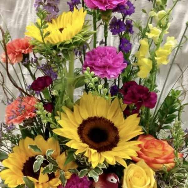 Tall mixed flower arrangement with sunflowers, roses, and purple blooms in a basket
