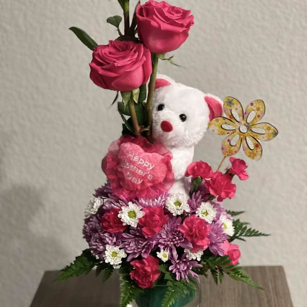 Pink rose arrangement with a teddy bear and flowers in a glass vase
