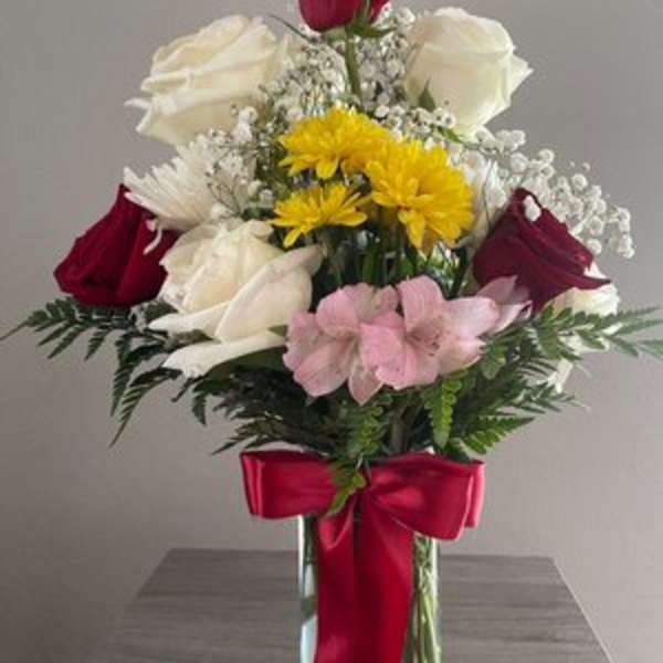 Mixed bouquet of roses, daisies, and pink flowers in a glass vase with a red bow