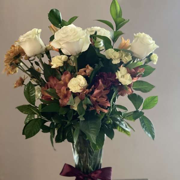 Bouquet of white roses and mixed flowers in a glass vase with a purple ribbon