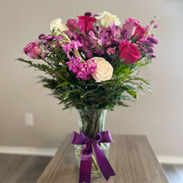 Mixed pink and white bouquet in a clear glass vase with a purple ribbon