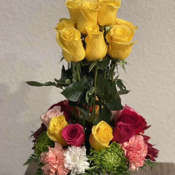 Tall bouquet of yellow and pink roses with carnations in a white vase
