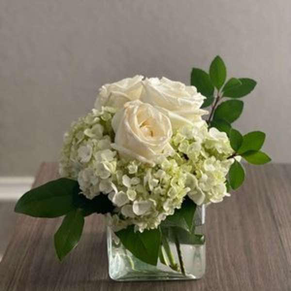 White roses and pale hydrangeas in a clear square vase