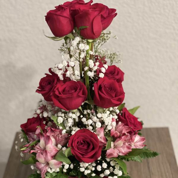 Tiered bouquet of red roses and pink flowers in a glass vase with a red ribbon