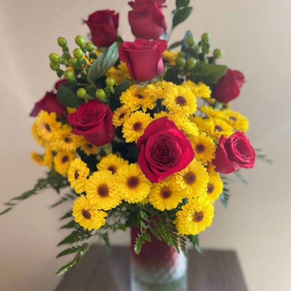 Bouquet of red roses and yellow daisies in a clear glass vase