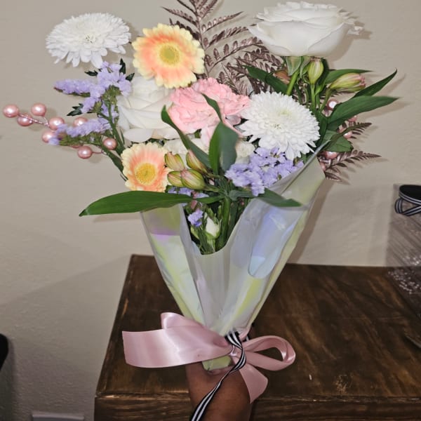 Bouquet of mixed pastel flowers wrapped in translucent paper with a pink ribbon