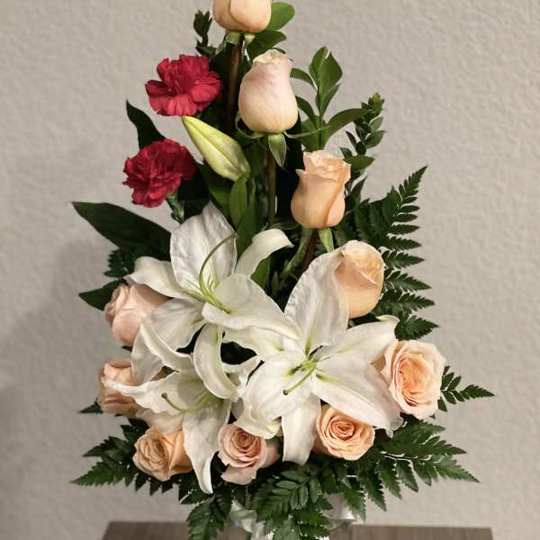 Bouquet of peach roses, white lilies, and red carnations in a glass vase