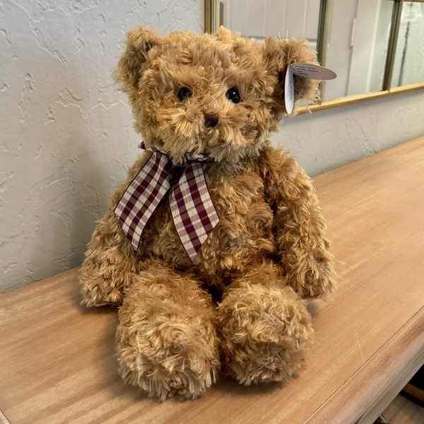 Plush teddy bear with a plaid ribbon sitting on a wooden surface