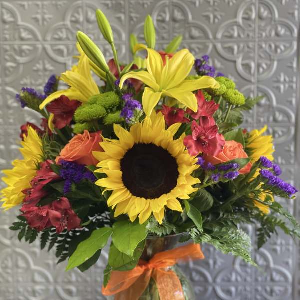 Bouquet of sunflowers, lilies, roses, and purple filler in a glass vase