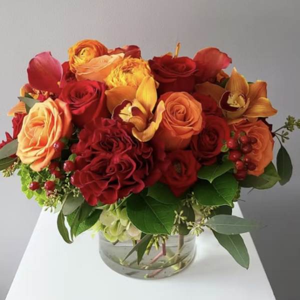 Bouquet of red and orange roses with orchids in a glass vase