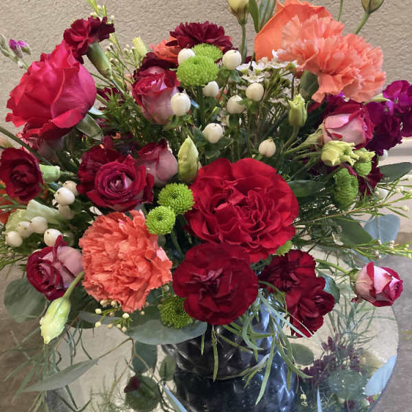 Mixed bouquet of red roses, carnations, and green button mums in a glass vase