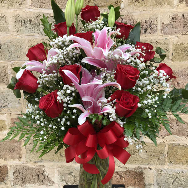 Red roses and pink lilies in a glass vase with a red ribbon