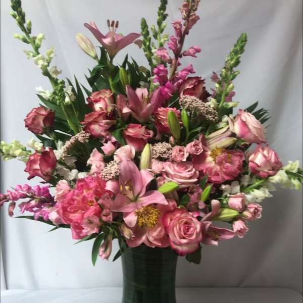 Pink mixed flower arrangement in a tall green vase