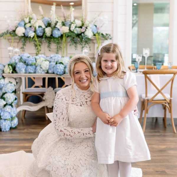 Bride and young girl in white dresses posing before blue and white floral decor