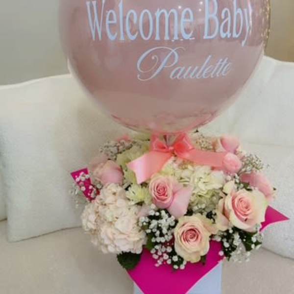 Pink balloon above a pastel flower arrangement with a baby name message