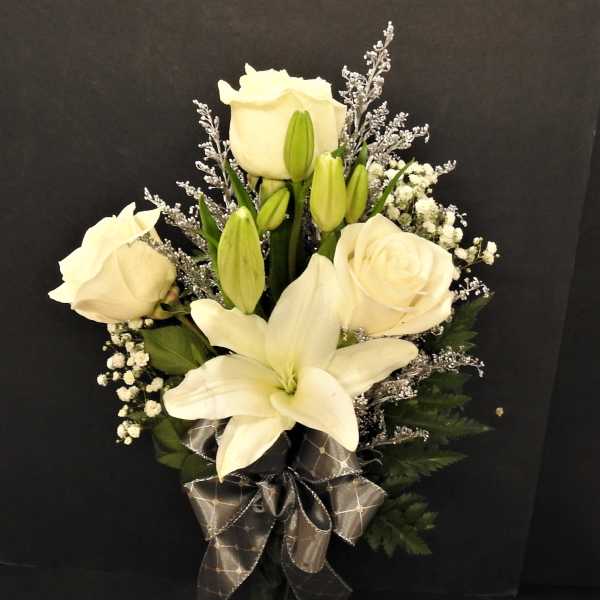 White roses and lilies arranged in a glass vase with a dark ribbon
