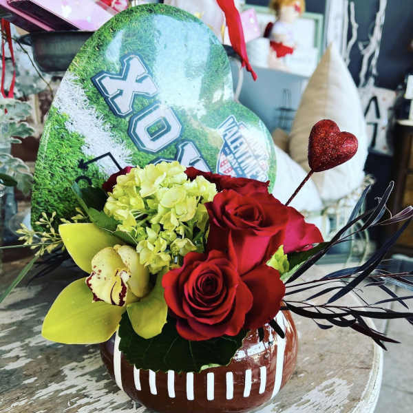 Red roses and yellow orchids in a football-shaped vase with a glitter heart pick