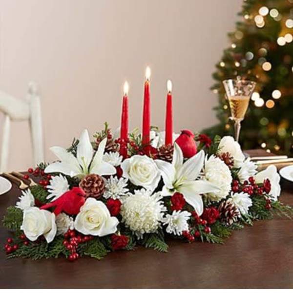 Holiday centerpiece with white flowers, red candles, and pinecones on a table