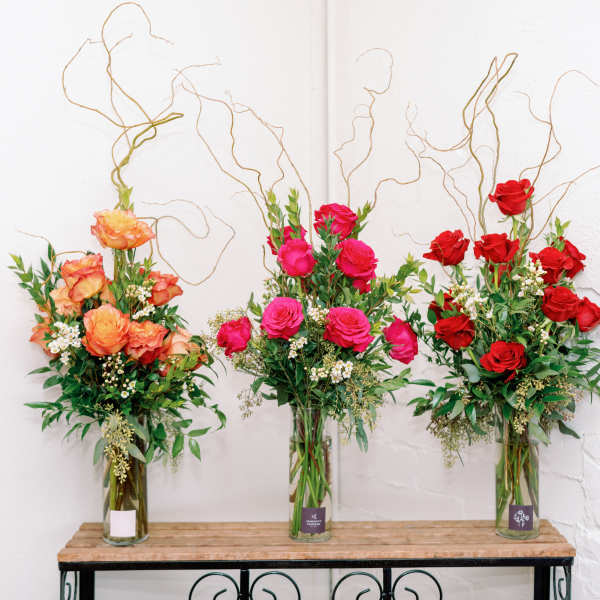 Three tall rose arrangements in glass vases with curly branches