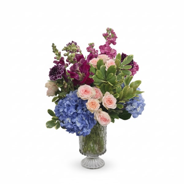Bouquet of blue hydrangeas, pink roses, and purple flowers in a glass vase