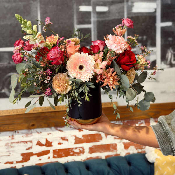 Mixed bouquet in a black vase with red, pink, and peach flowers