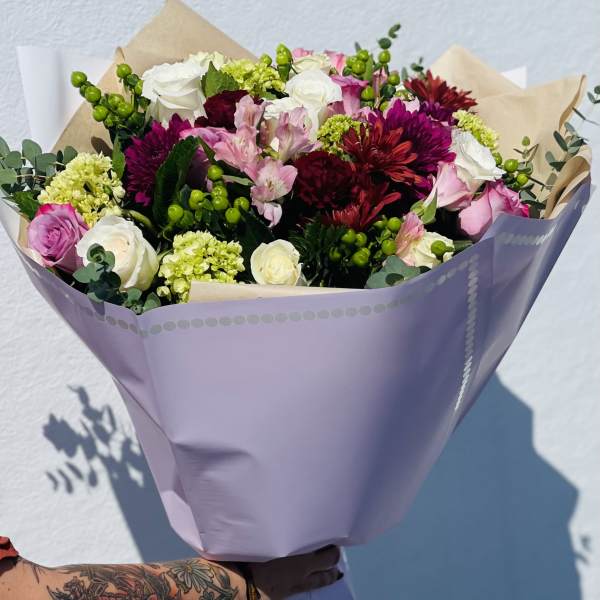 Mixed bouquet of pink, white, and burgundy flowers wrapped in lavender paper