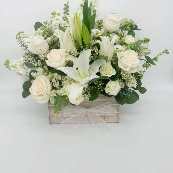 White roses and lilies arranged in a wooden box with a sheer white bow.