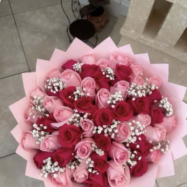 Round bouquet of pink and red roses with white filler flowers wrapped in pink paper