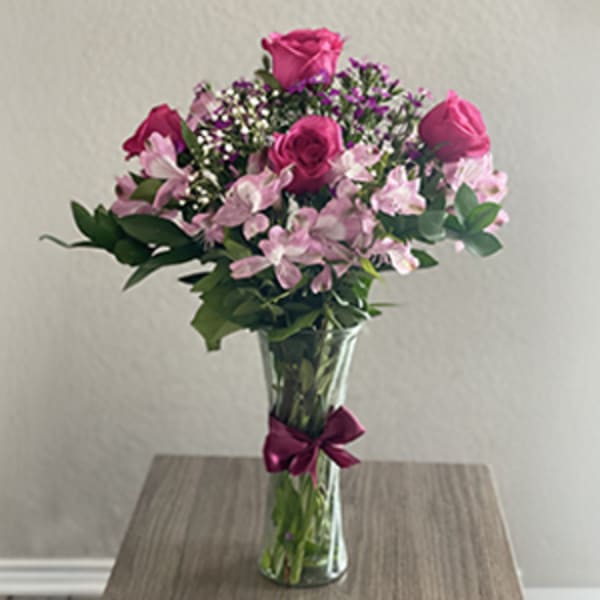 Pink roses and alstroemeria in a clear glass vase with a ribbon