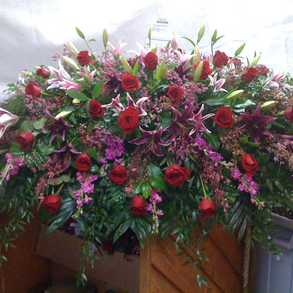 Large casket spray with red roses, lilies, and pink filler flowers