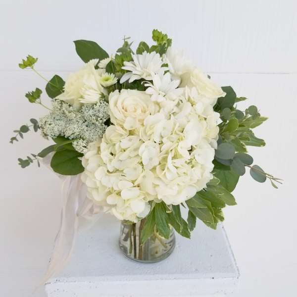 White floral bouquet in a glass vase with green foliage