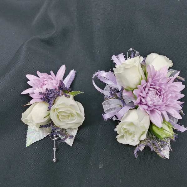 Two lavender and white floral corsages on a dark fabric background