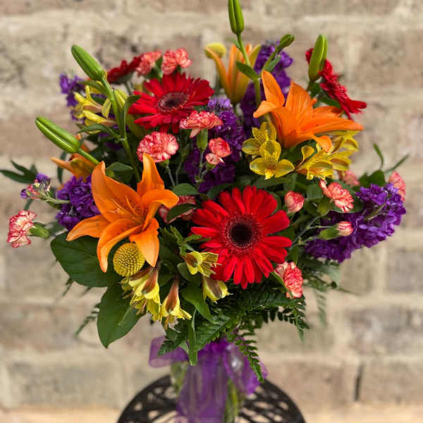 Colorful bouquet with orange lilies, red gerbera daisies, and purple flowers in a vase