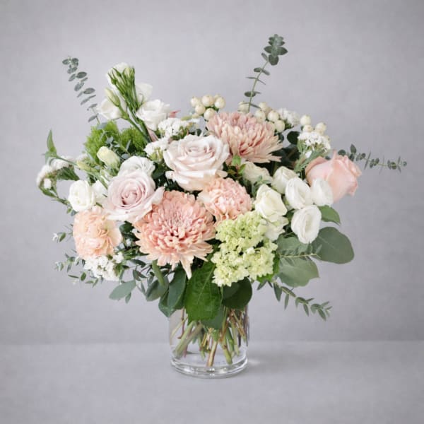 Pastel bouquet of roses, chrysanthemums, and white blooms in a glass vase