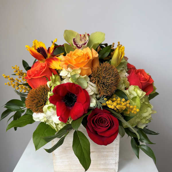 Mixed bouquet with red, orange, and yellow flowers in a white box