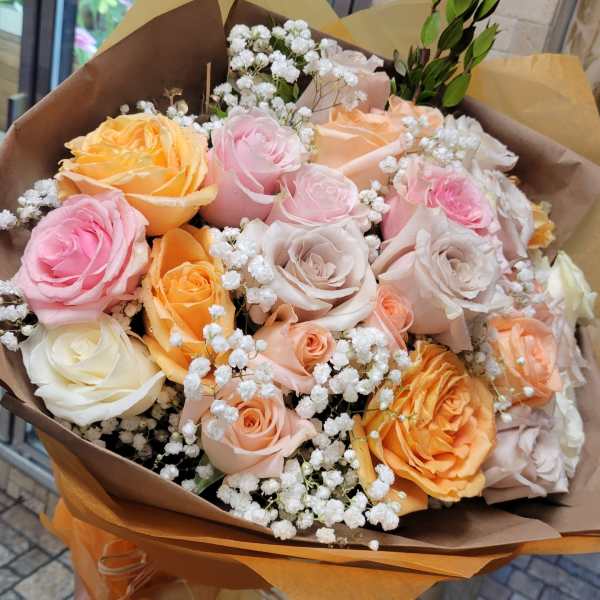 Handheld bouquet of pink, peach, and cream roses wrapped in brown paper