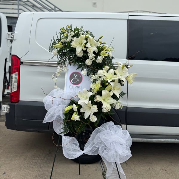 White lily floral wreath with large white bows on a stand