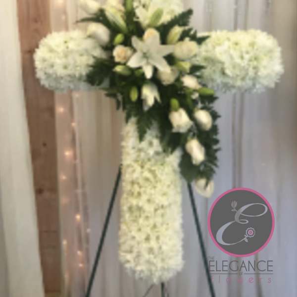 White floral cross on a stand with lilies and clustered white blooms