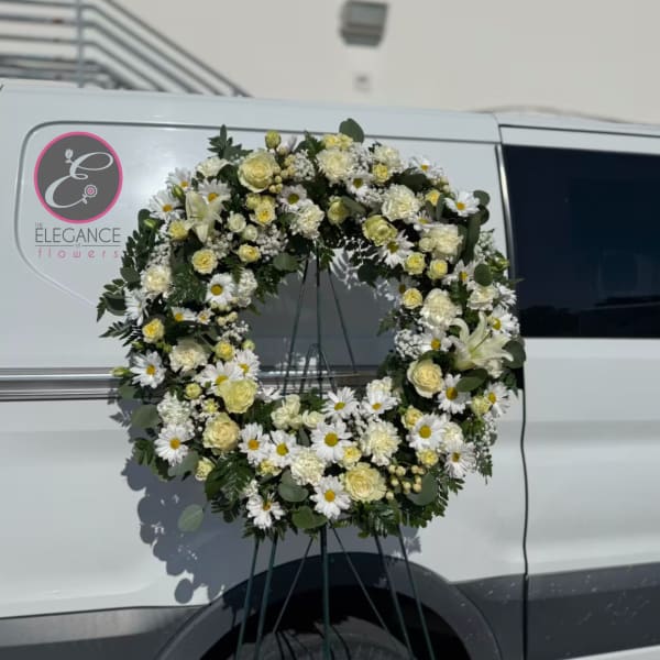 Large white floral wreath on a stand with daisies and roses