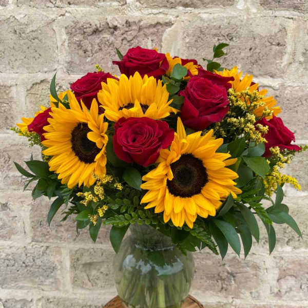 Bouquet of red roses and yellow sunflowers in a glass vase