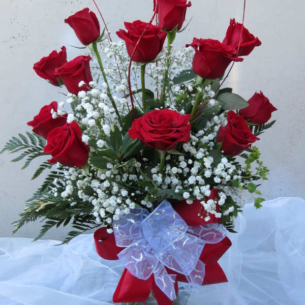 Red roses arranged in a clear glass vase with white baby's breath and a red ribbon bow