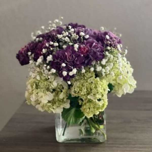 Purple and green hydrangea bouquet in a clear square vase