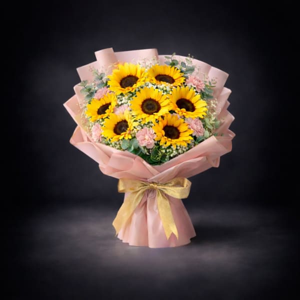 Bouquet of sunflowers and pink flowers wrapped in blush paper with a gold ribbon