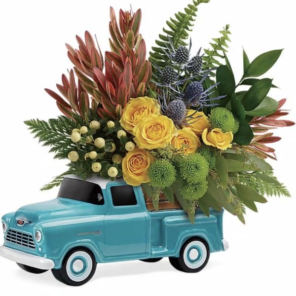 Yellow and green mixed flowers arranged in a turquoise ceramic truck-shaped container