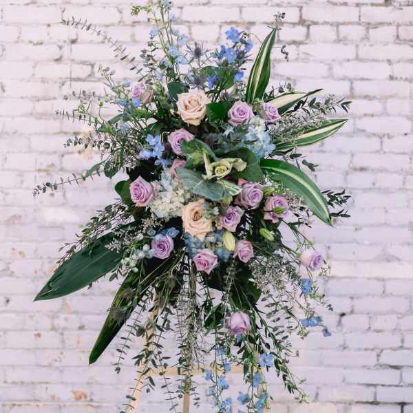 Tall floral spray with lavender and blue flowers on an easel