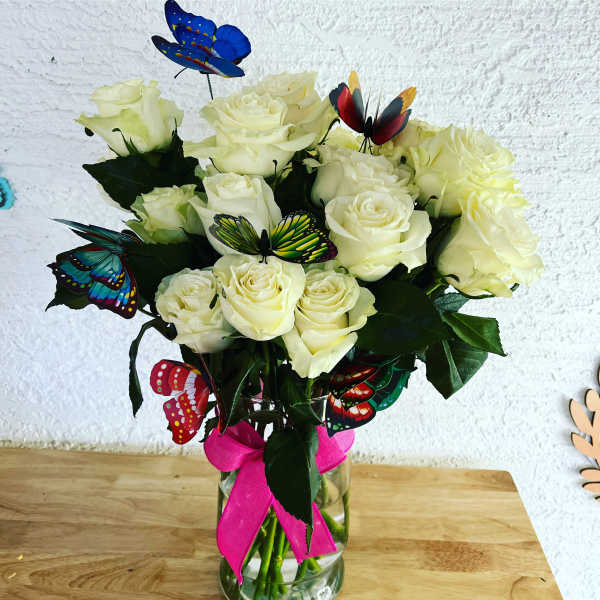 White rose bouquet in a glass vase with colorful butterfly picks
