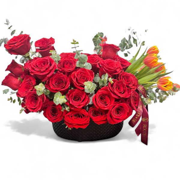 Red roses arranged in a black basket with orange tulips