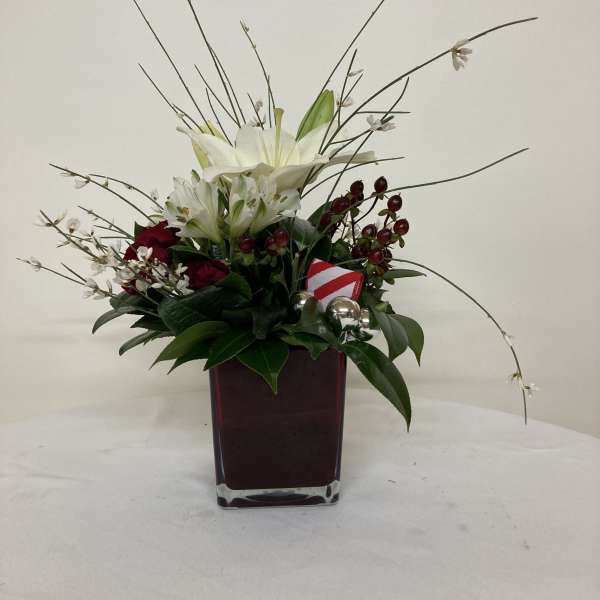 White lilies and red roses in a square glass vase with holiday accents