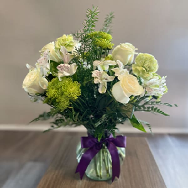 Bouquet of cream roses and green carnations in a glass vase with a purple ribbon