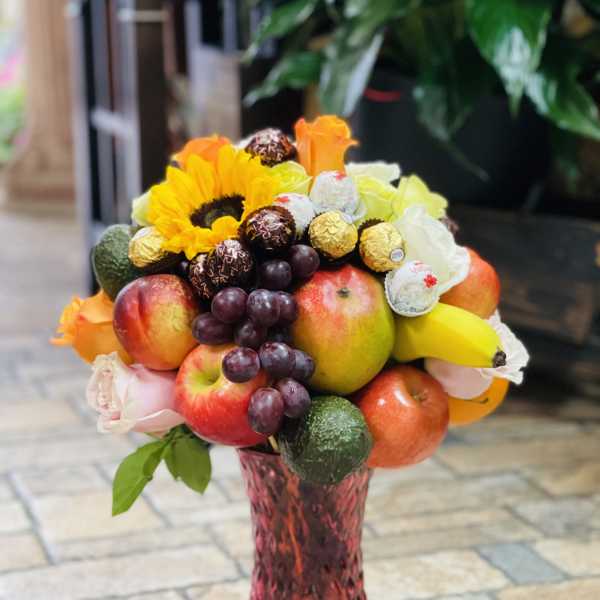 Fruit bouquet with sunflowers, roses, grapes, apples, bananas, and chocolates in a pink vase